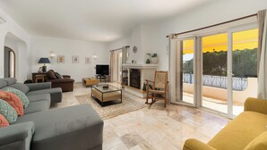 A spacious living room with a fireplace, a television, and a balcony with a yellow view. - Casa Vale da Ana Carvoeiro with private pool (Carvoeiro)