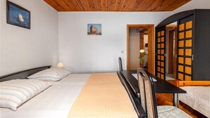 A room with two beds, a wooden ceiling, and a painting of a building.
