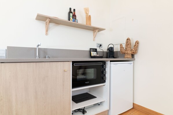 A compact kitchen with a built-in microwave, a small refrigerator, and a wooden shelf above the counter.