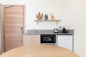 A compact kitchen with a wooden door, a built-in oven, a dishwasher, and a shelf with kitchen utensils and bottles.
