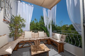 A balcony with a cushioned seating area, a potted plant, and a patterned rug.