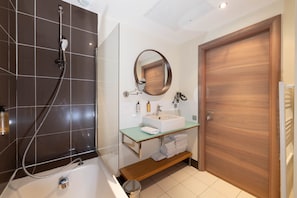 A modern bathroom with a bathtub, a glass-enclosed shower, a wooden door, and a mirror above the sink. - Cocoon Balinais with Terrace – 2-Bed Mandara Beach (Juan-les-Pins)