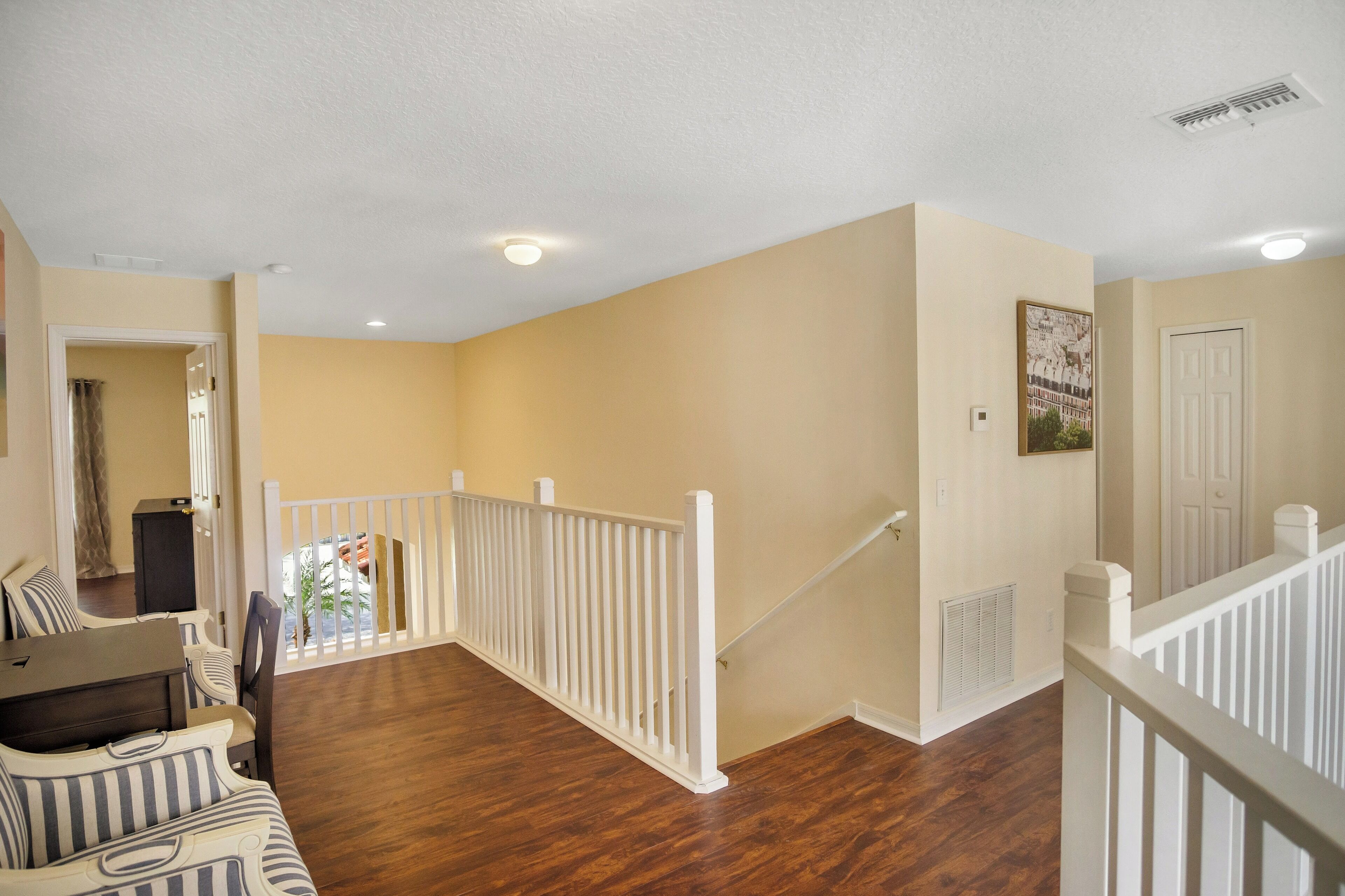 A spacious living area with a wooden floor, white railing, and a staircase leading to another level.