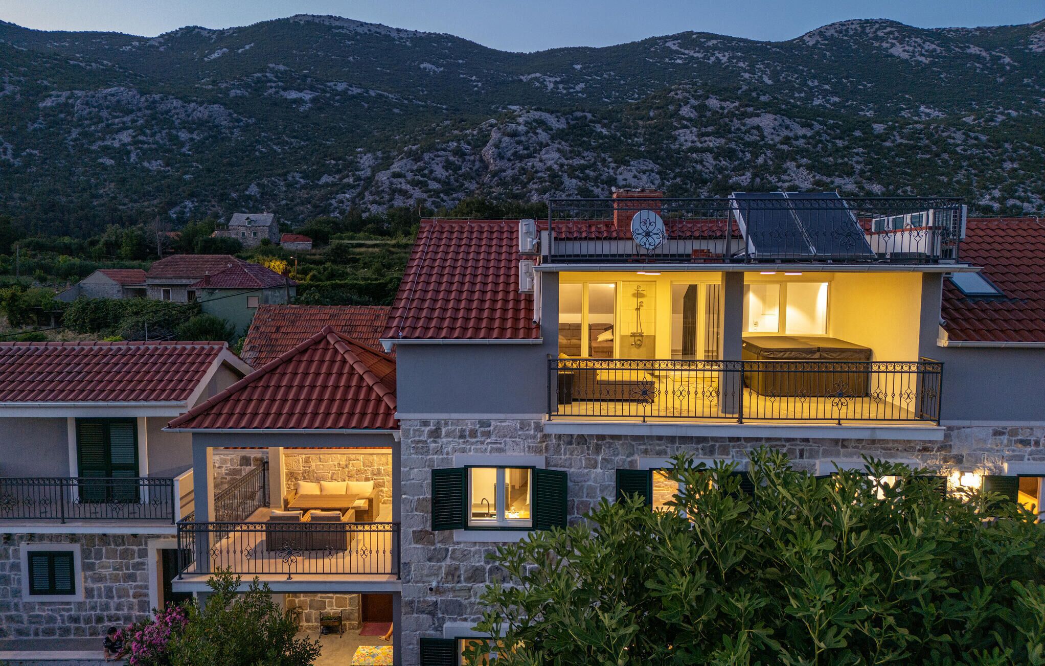 Una casa a due piani con un balcone, pareti in pietra e vista su un paesaggio montuoso.