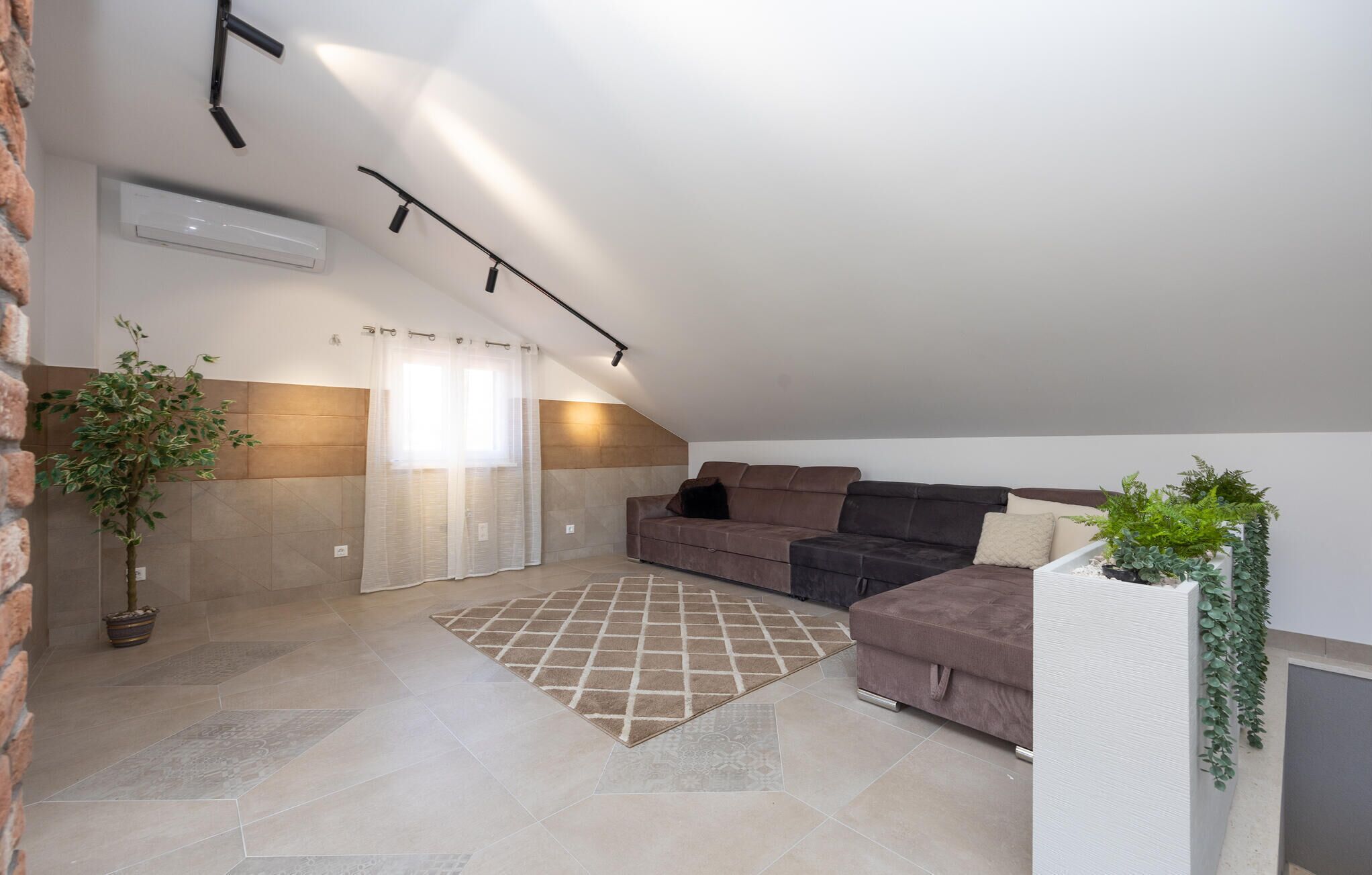 A spacious attic room with a brown sofa, a patterned rug, and a potted plant.