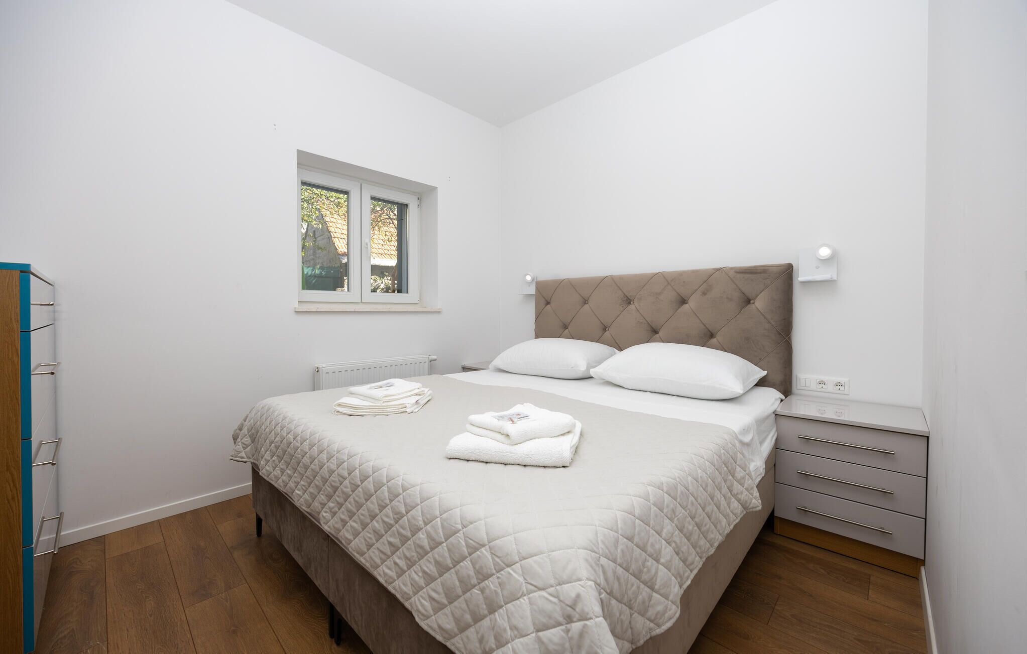 Ein Schlafzimmer mit Bett, Fenster, Heizkörper, Nachttisch und Kleiderschrank.