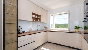 A modern kitchen with a large window, built-in shelves, and a view of greenery outside. - Nice home in Cvrljevo (Cvrljevo)