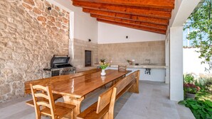 A spacious outdoor kitchen with a large wooden table, built-in grill, and stone walls. - Nice home in Cvrljevo (Cvrljevo)
