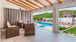 A spacious balcony with a pool, wicker furniture, and a view of a green hillside. - Nice home in Cvrljevo (Cvrljevo)