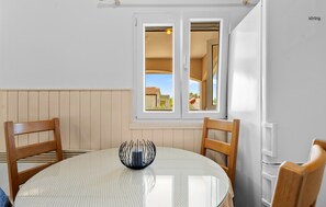 A dining area with a round table, two wooden chairs, a glass vase, and a window with a view of a house and a silo.