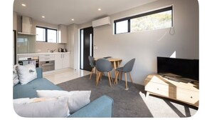 Una sala de estar moderna con un sofá azul, un televisor y un comedor con sillas y una mesa.