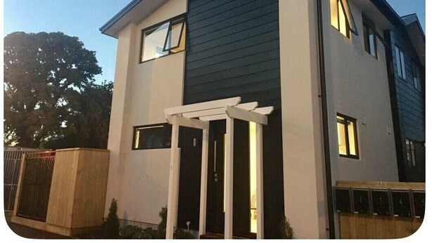 Una casa moderna de dos pisos con fachada blanca y revestimiento oscuro, que incluye un porche cubierto y un buzón visible.