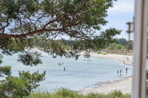 Une plage oĂč lâon voit des gens se baigner et se promener le long du rivage, entourĂ©e dâarbres et sous un ciel dĂ©gagĂ©.