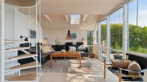 Un salon moderne avec un plafond en bois, un canapé noir, une table basse en bois et de grandes fenêtres donnant sur un paysage verdoyant.