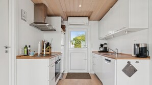 Une cuisine compacte avec des meubles blancs, un plan de travail en bois, un four encastré, une machine à café et une vue à travers une porte.