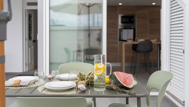 A dining table set with plates, glasses, a pitcher with lemon slices, and a watermelon.