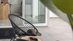 A modern outdoor seating area with a wicker chair and a hat, a glass door leading to a kitchen, and a 'Home' mat at the entrance.
