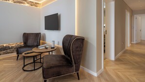 A modern living room with two dark armchairs, a small round table, and a flat-screen TV mounted on the wall.