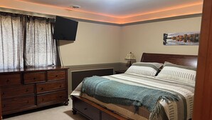 Un dormitorio con cama, cómoda, mesita de noche, lámpara y un cuadro en la pared.