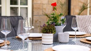 A table set for a meal with wine glasses, plates, and a potted plant with red flowers.