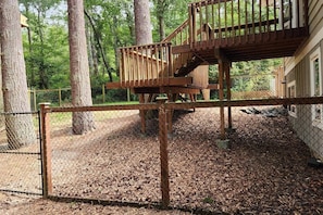A wooden deck with a staircase leading to a higher level, surrounded by a chain-link fence and trees.