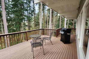 A wooden deck with a grill and a table with chairs, surrounded by tall trees.