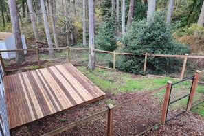 A wooden deck with a metal railing, surrounded by a forested area.