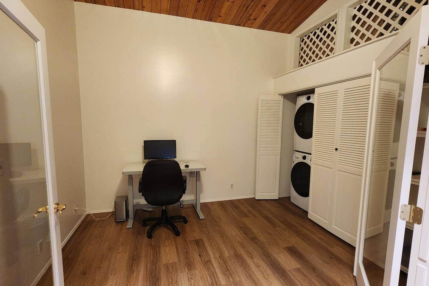 A room with a desk, chair, and a washing machine.