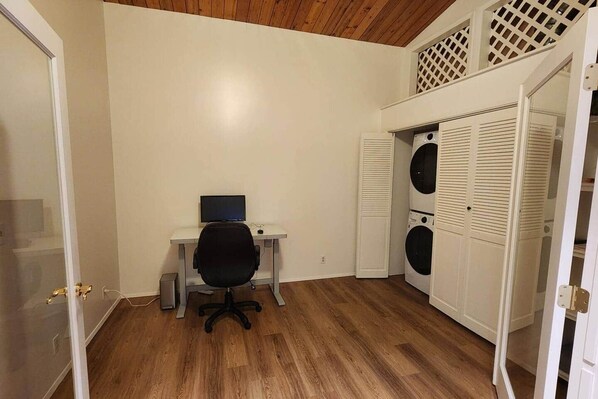 A room with a desk, chair, and a washing machine.