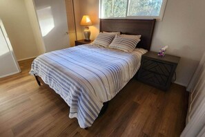 A bedroom with a bed, a nightstand, a lamp, and a window.