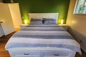 A bed with a striped bedspread, two bedside lamps, a white headboard, and a window with a view of trees.