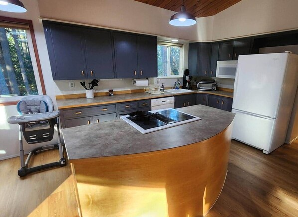 A modern kitchen with dark cabinets, a central island, a built-in microwave, and a white refrigerator.