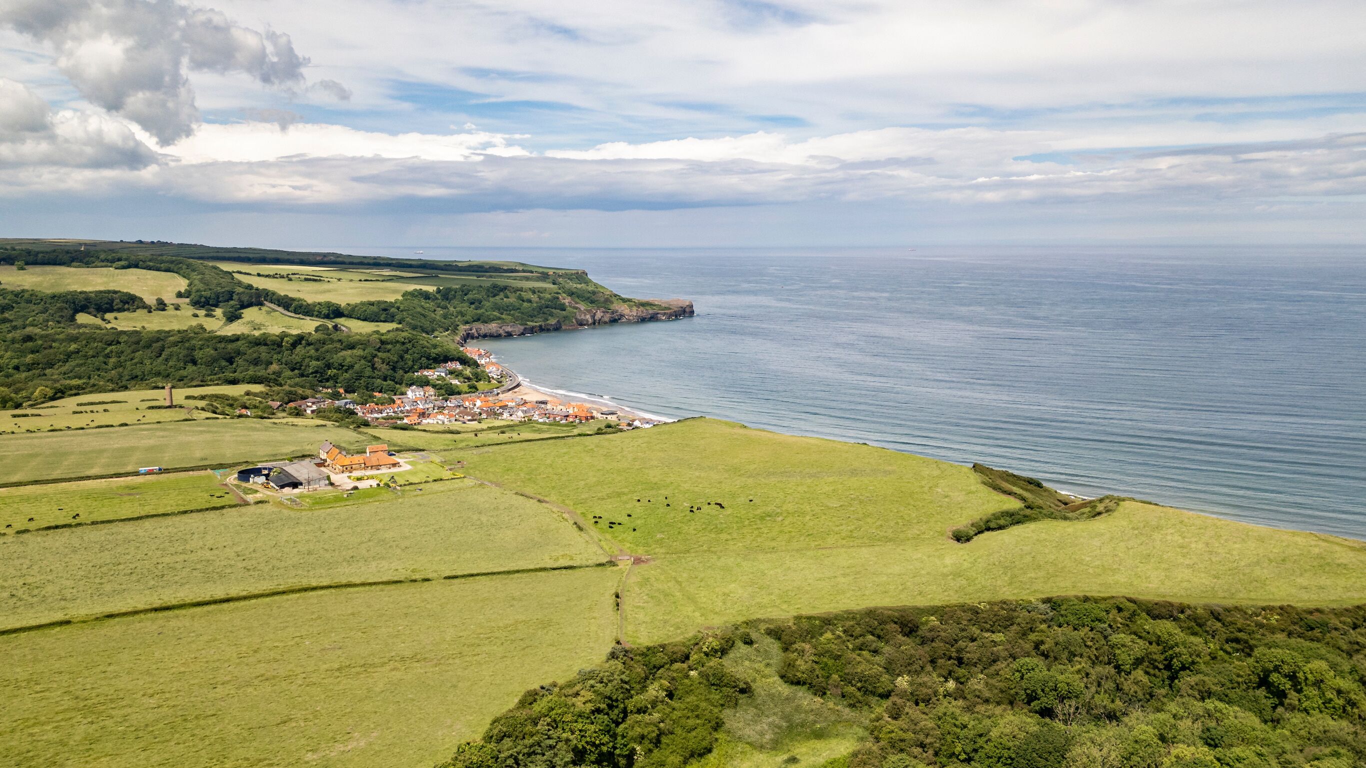 A coastal village with green fields, a beach, and a sea view.