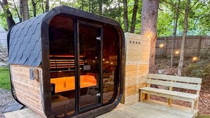 A wooden cabin with a glass door, a bench, and a wooden deck. - SaunaHaus | Log Cabin + Private Sauna by the Brook (Lincoln)