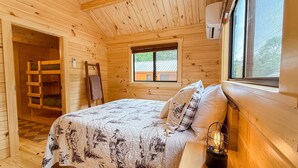 A wooden cabin room with a bed, a ladder, a window, and a wall-mounted heater. - SaunaHaus | Log Cabin + Private Sauna by the Brook (Lincoln)