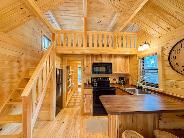 L’intérieur d’une cabane en bois comprend une cuisine, un coin repas et un escalier.