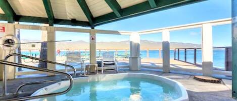 A covered outdoor swimming pool with a view of the ocean and mountains in the background.