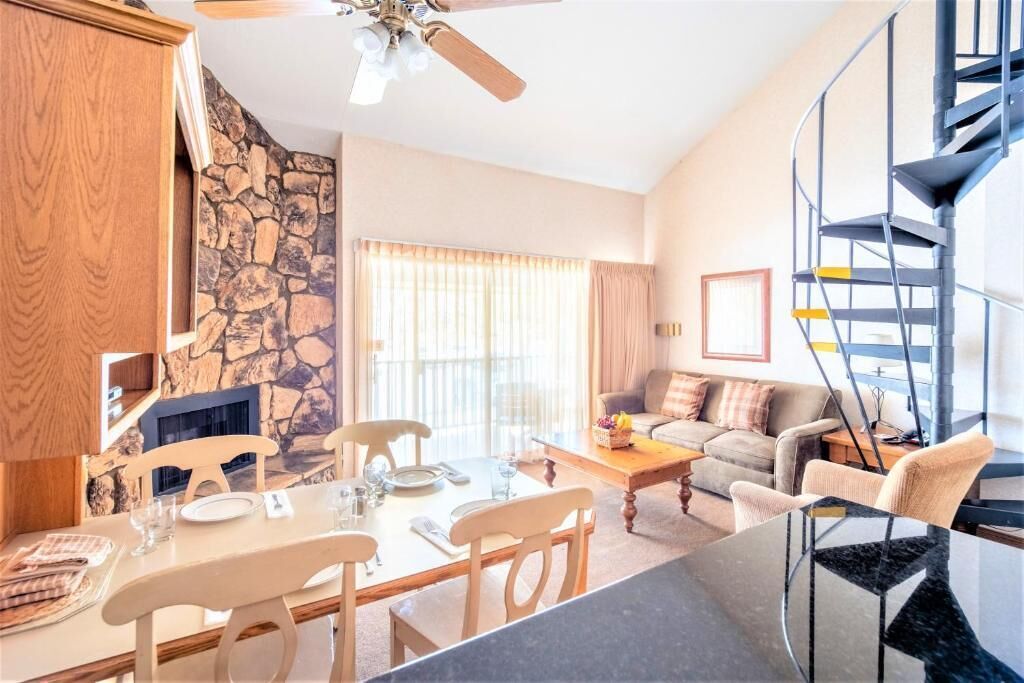 A modern living room with a stone wall, a dining area with wooden furniture, and a spiral staircase.