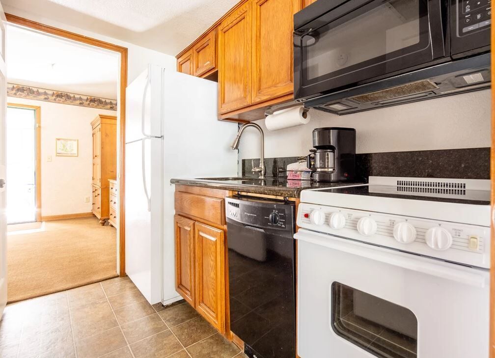 A kitchen with wooden cabinets, a white refrigerator, a black dishwasher, a white stove, and a black microwave.