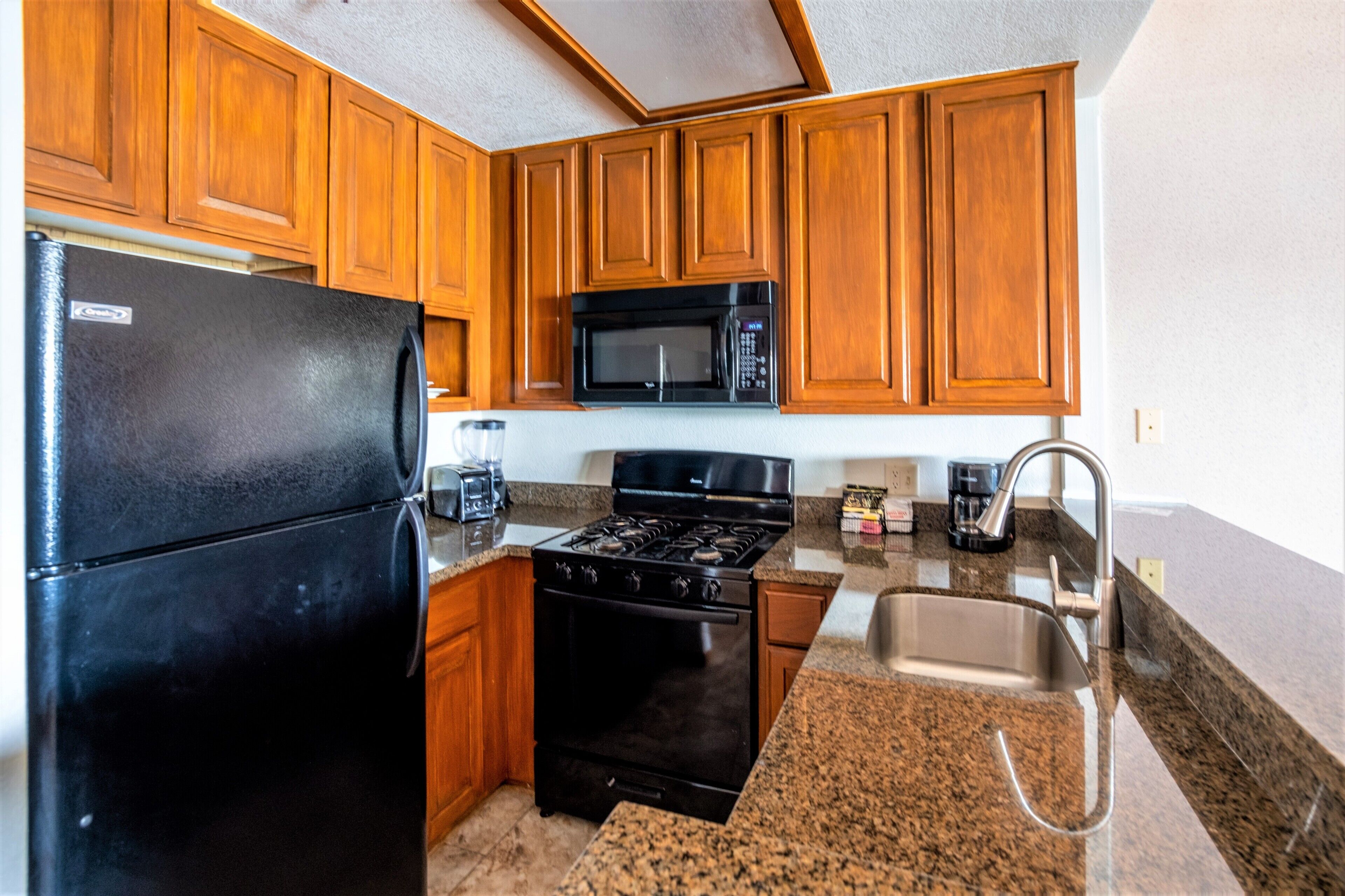 A kitchen with wooden cabinets, a black refrigerator, a microwave, a stove, and a sink.