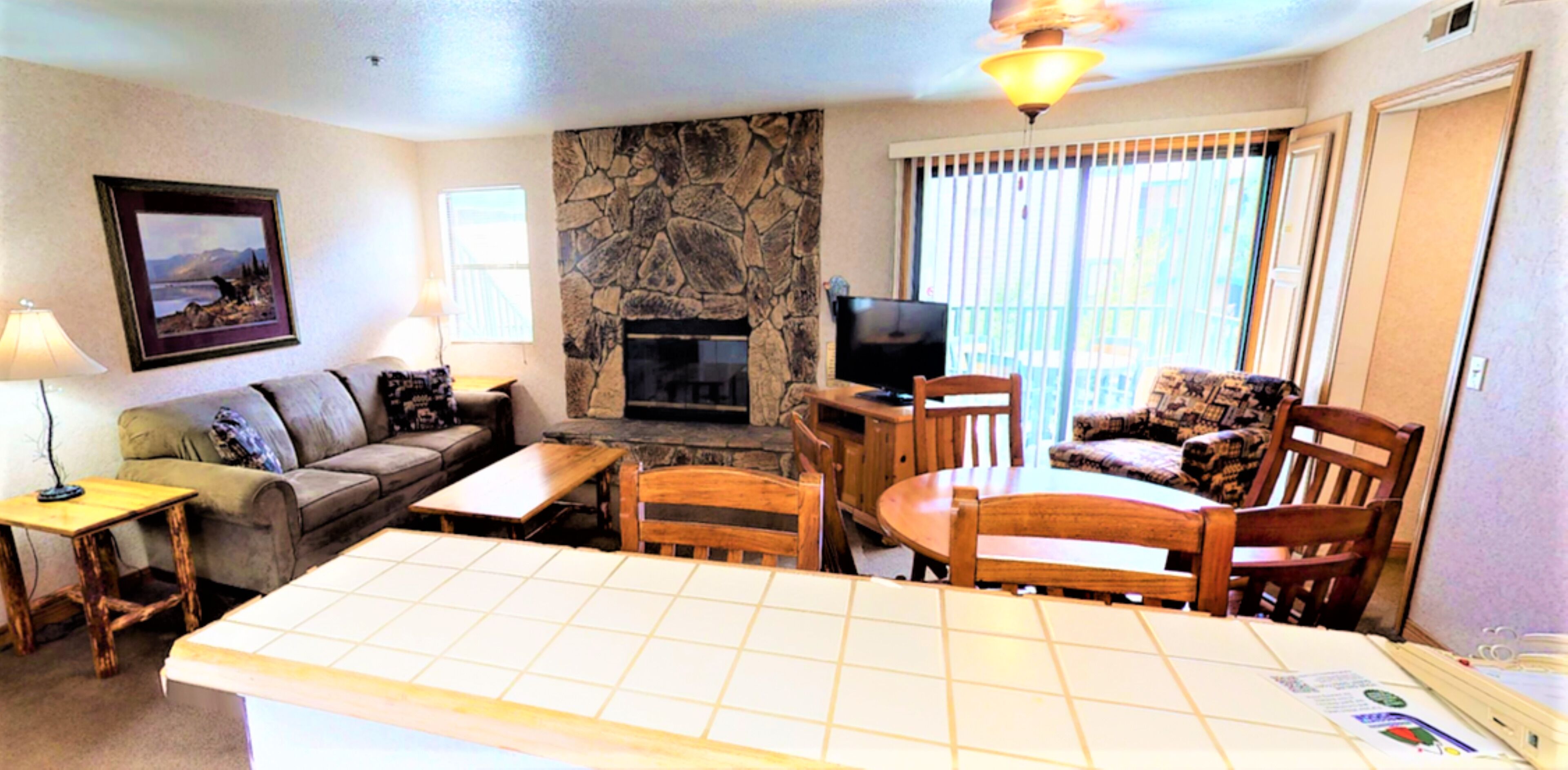 A living room with a stone fireplace, a television, a dining table with chairs, a sofa, and a lamp.