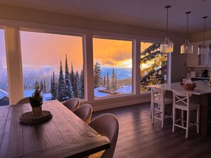 Une cuisine moderne avec de grandes fenêtres, une table à manger en bois et une vue sur un paysage enneigé.