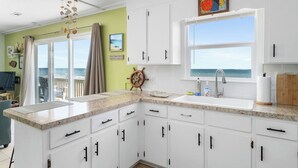 Une cuisine avec des meubles blancs, un plan de travail en granit, une grande fenêtre donnant sur la mer et un élément décoratif en forme de barre de timon de navire.