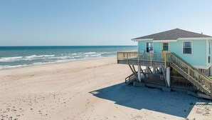 Une maison de plage dotée d’une terrasse en bois et d’un escalier menant à un balcon avec vue sur l’océan.