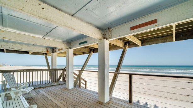 Une terrasse en bois avec des chaises blanches donnant sur une plage.