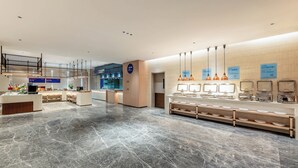 Un hall d’hôtel moderne comprenant un comptoir d’accueil, un espace salon et un buffet.