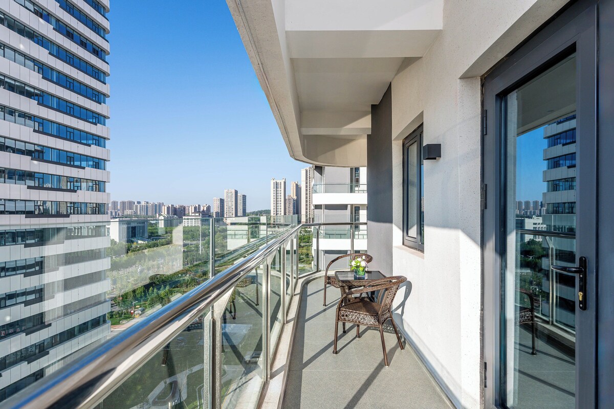 A balcony with a glass railing, a table with chairs, and a view of surrounding buildings.