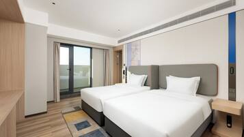 Habitación de hotel moderna con dos camas, suelo de madera, un ventanal grande y una puerta corredera que da a un balcón.