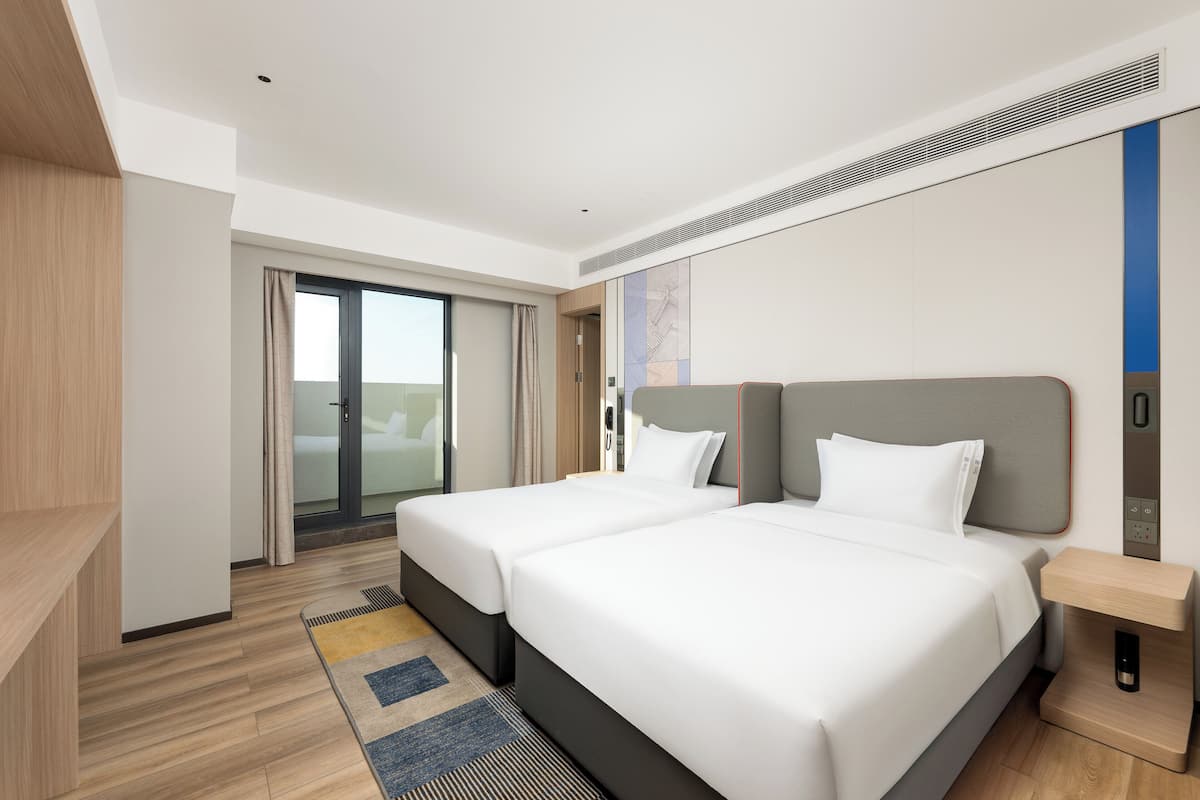 A modern hotel room with two beds, a wooden floor, a large window, and a sliding door leading to a balcony.