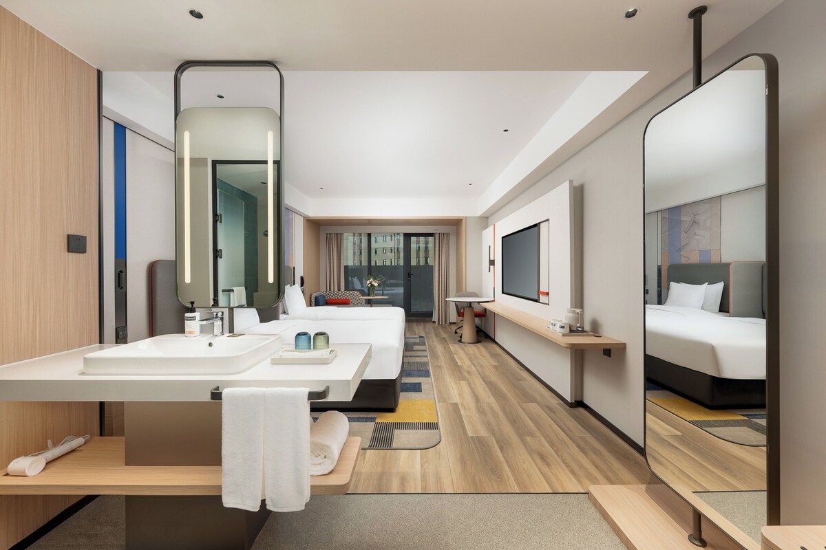 A modern hotel room with a large bed, a separate sitting area, a large mirror, and a television.